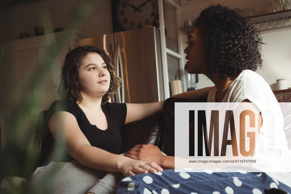 IMAGO Creative: Pride Month 2022, Engagement der Jugendlichen Lesbian couple holding hands while sitting on a couch Lesbian couple holding hands while sitting on a couch at home, model released, , property released, Vancouver, Canada, 06.03.2017, 992996.jpg, home, house, household, homey, apartment, domicile, abode, authentic, real life, domestic life, hold, holding, hands, close, closeness, couch, couple, relationship, adult, lesbian, lesbian couple, girlfriend, look, talk, talking, conversation, looking, homosexual, partner, gay, youth, love, lover, affection, lifestyle, together, leisure, bonding, romance, romantic, sensuality, passion, intimate, milleninial
