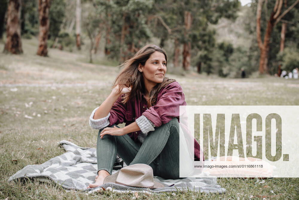 IMAGO Creative: Jahreszeit Fr?hling, Picknick Cheerful female sitting on plaid on meadow in woods and looking away while enjoying picnic in Australia