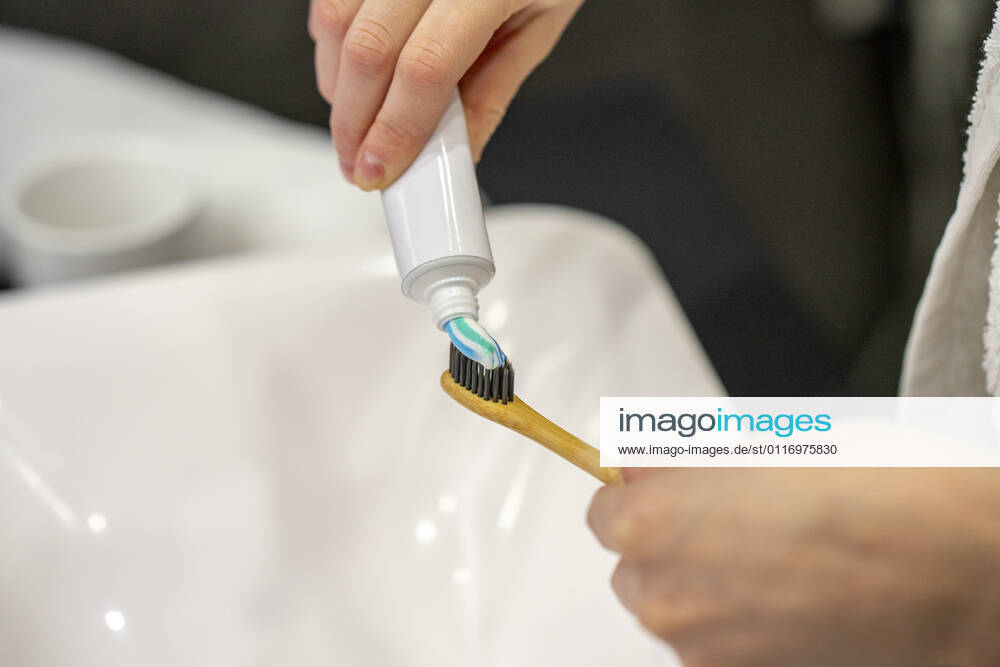 Woman taking toothpaste on toothbrush at home model released Symbolfoto property released VPIF03822