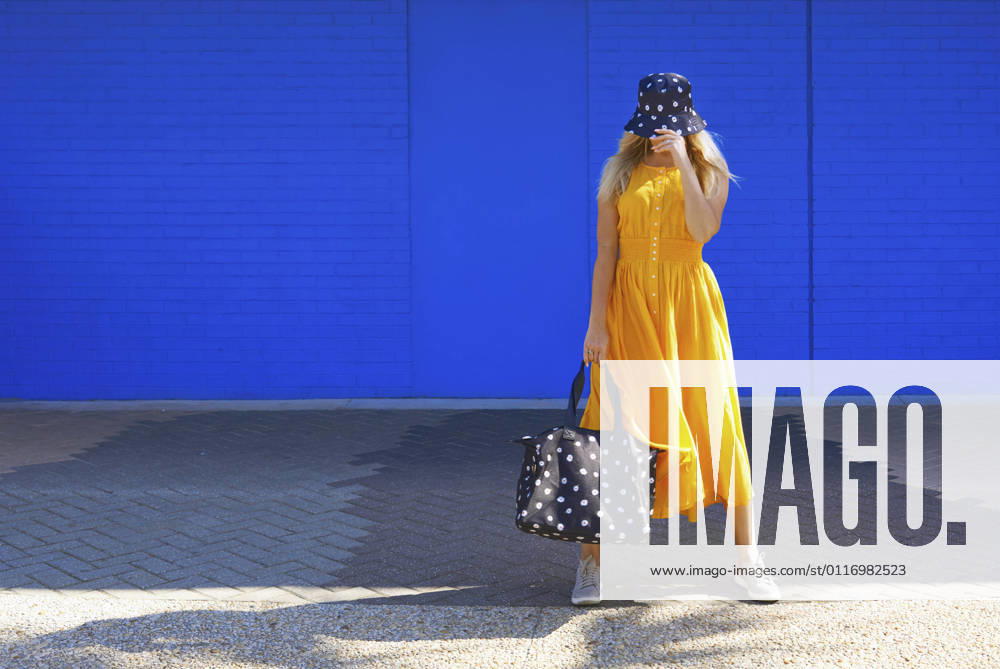 Mature woman with duffel bag and bucket hat in front of blue wall model released Symbolfoto AZF00274