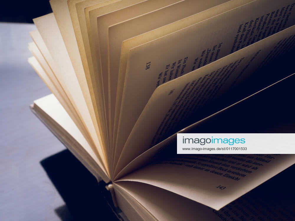 Geöffnetes und gefächertes Buch vor dunklem Hintergrund mit Textfreiraum