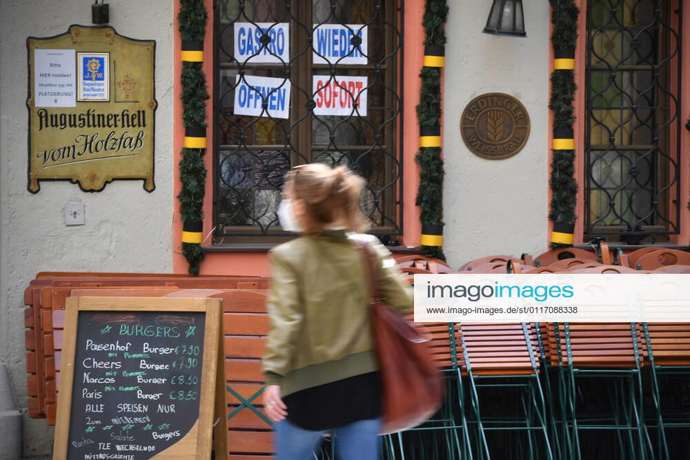 Themenbild: Coronavirus Pandemie Folgen fuer die Gastronomie: GASTRO WIEDER OEFFNEN SOFORT Im Fenster eines bayerischen Restaurants in Muenchen fordern die Eigentuemer die sofortige Oeffnung der Gastronomie. Uebereinander gestapelte Stuehle und Tische lehnen an der Hauswand. Passanten gehen mit Mundschutz,Maske vorbei.