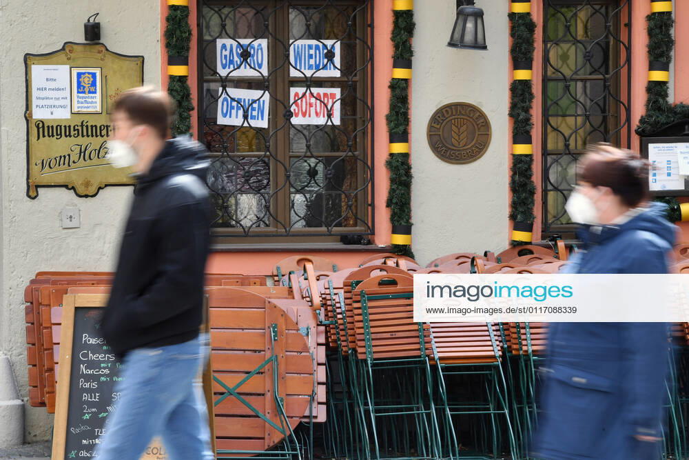 Themenbild: Coronavirus Pandemie Folgen fuer die Gastronomie: GASTRO WIEDER OEFFNEN SOFORT Im Fenster eines bayerischen Restaurants in Muenchen fordern die Eigentuemer die sofortige Oeffnung der Gastronomie. Uebereinander gestapelte Stuehle und Tische lehnen an der Hauswand. Passanten gehen mit Mundschutz,Maske vorbei.