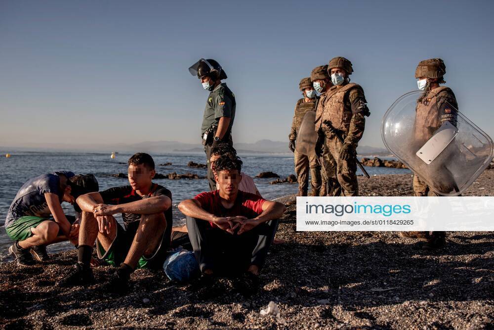 Morocco immigrants rest after reaching El Tarajal beach in the Spanish city of Ceuta, located in northern Africa, as members of the Spanish Army (R) and a member of the Guardia Civil (L) look on, 19 May 2021. Spain s Government considers that the massive arrival of some 8,000 irregular migrants to Ceuta from Morocco since 18 May is an assault on the border caused by the lack of control of the border by Morocco s Governmet and not a migratory crisis. Situation at El Tarajal beach in the Spanish city of Ceuta !ACHTUNG: NUR REDAKTIONELLE NUTZUNG!