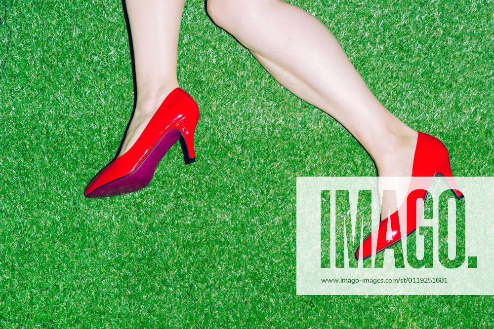 Top view of crop anonymous female in patent red shoes lying on grassy ground