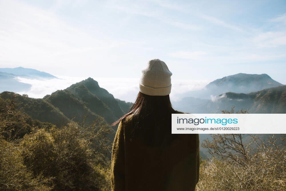 Back view of unrecognizable woman in warm clothes standing alone on viewpoint and looking at foggy mountain ridges covered fluffy clouds in Sequoia National Park under blue sky in USA, Model released