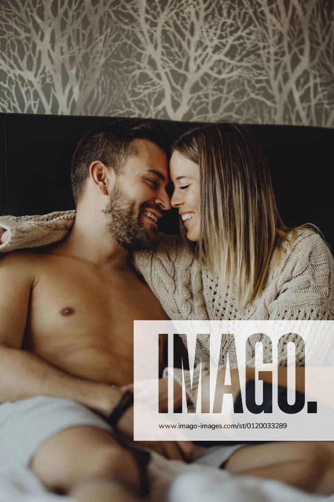 Cheerful young man and woman smiling and cuddling while lying on comfortable bed at home together, Model released