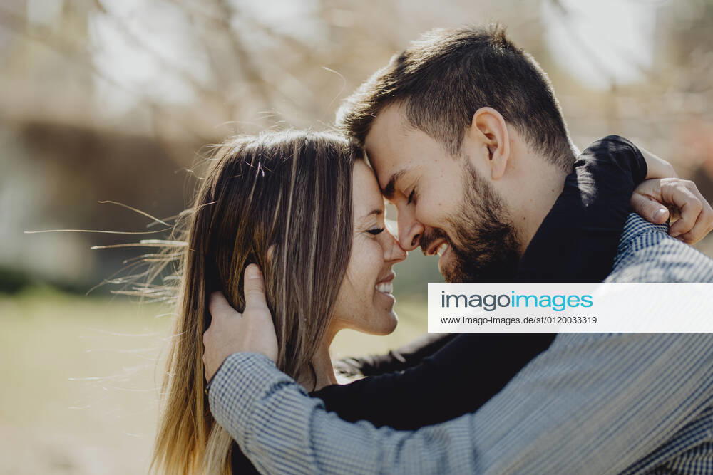 Bearded man hugging laughing woman while spending time on green lawn on street together, Model released