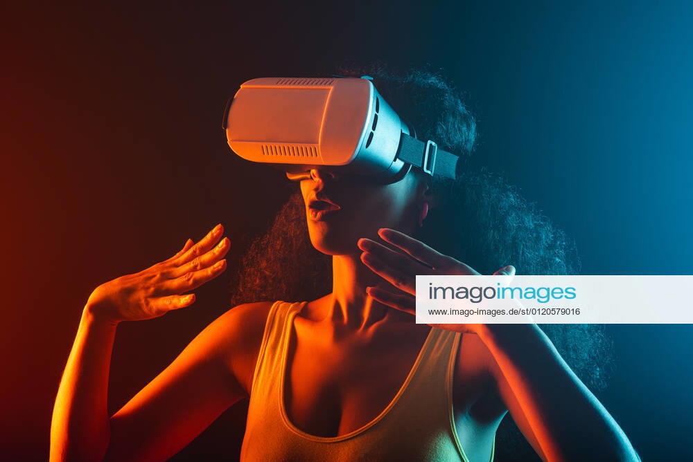 Anonymous astonished ethnic female with open mouth exploring virtual reality in headset on black background, Model released