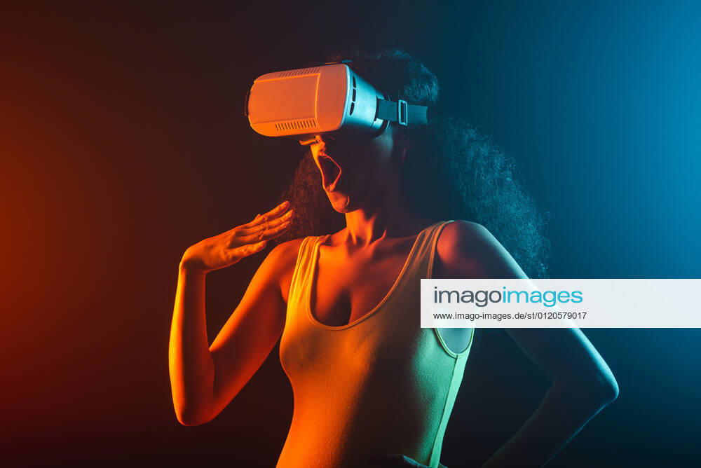 Anonymous astonished ethnic female with open mouth exploring virtual reality in headset on black background, Model released