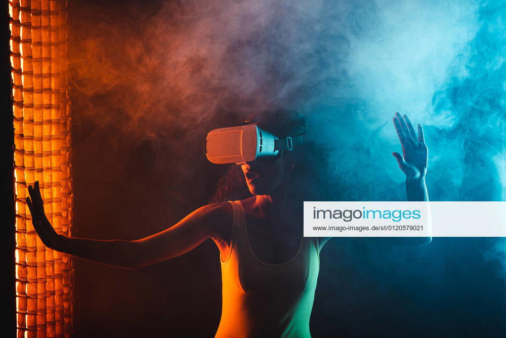 Anonymous astonished ethnic female with open mouth exploring virtual reality in headset on black background, Model released