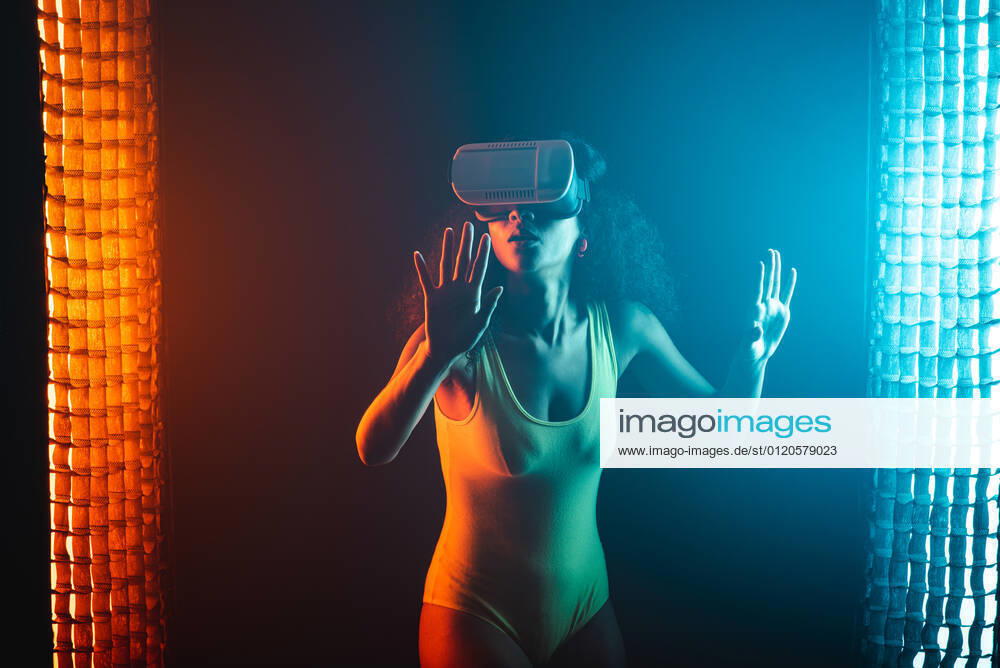 Anonymous astonished ethnic female with open mouth exploring virtual reality in headset on black background, Model released