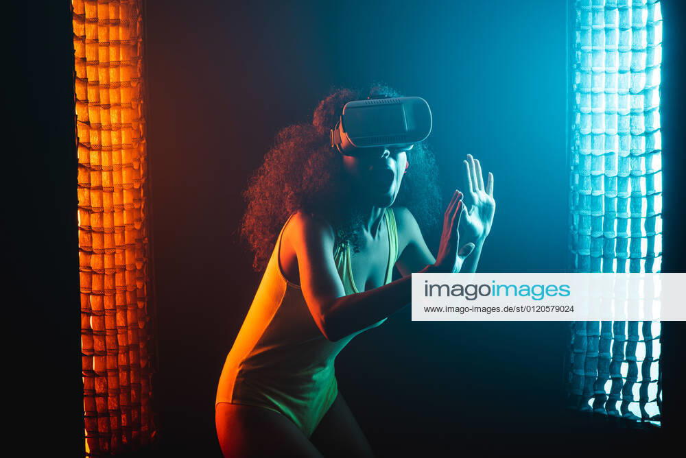 Anonymous astonished ethnic female with open mouth exploring virtual reality in headset on black background, Model released