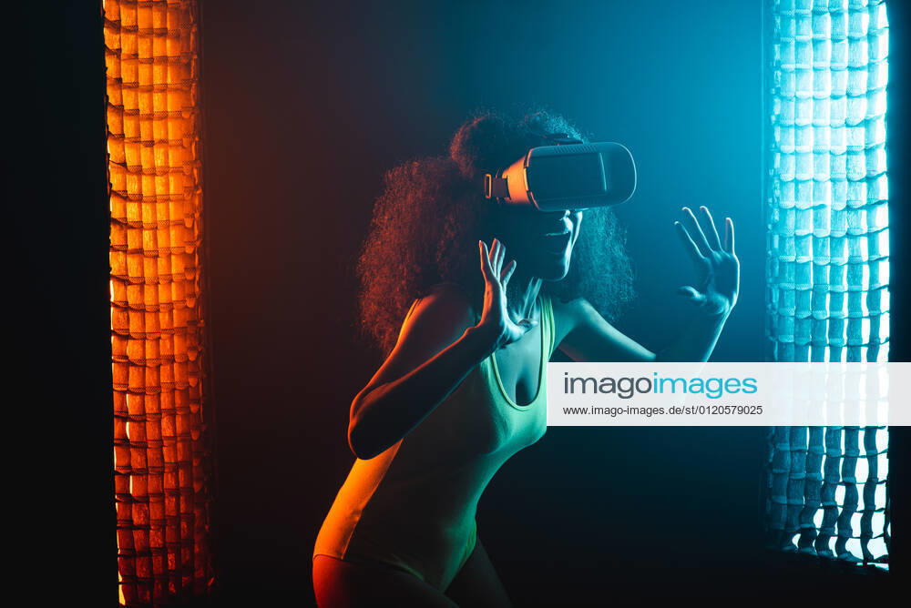 Anonymous astonished ethnic female with open mouth exploring virtual reality in headset on black background, Model released