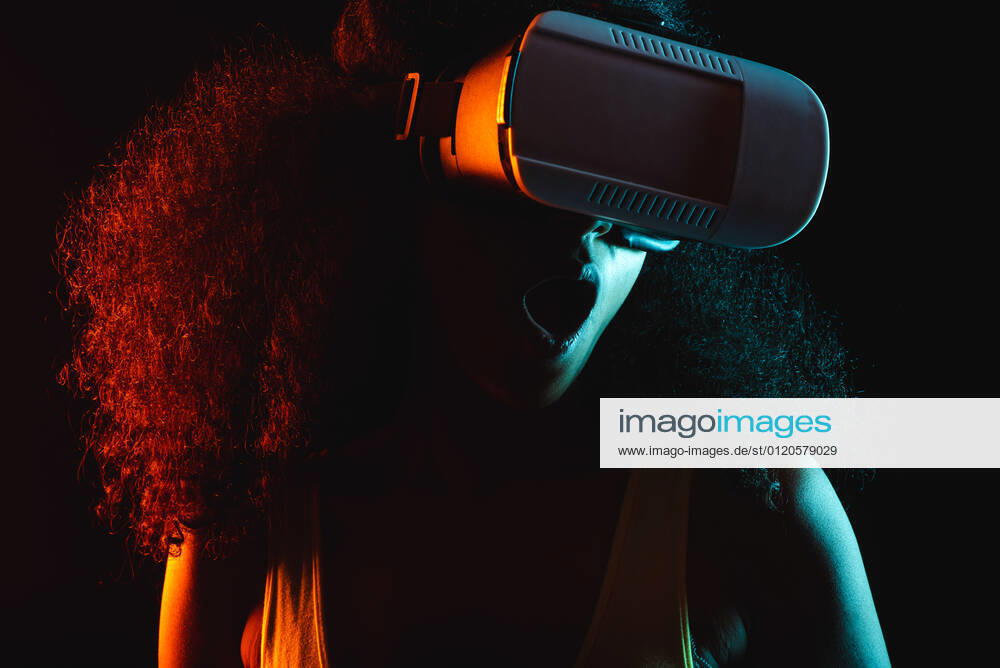 Anonymous astonished ethnic female with open mouth exploring virtual reality in headset on black background, Model released