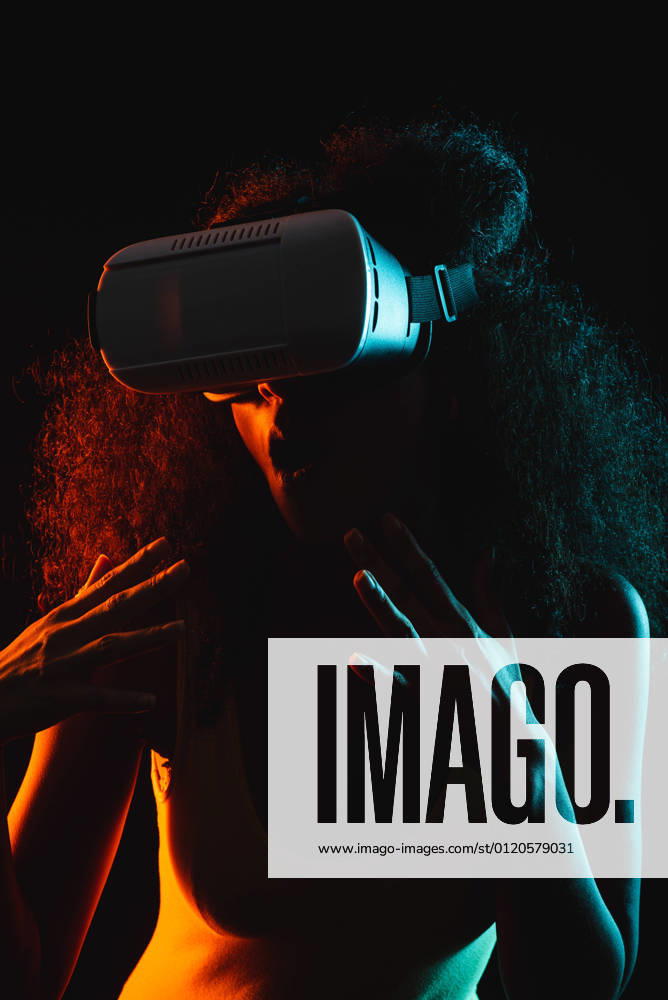 Anonymous astonished ethnic female with open mouth exploring virtual reality in headset on black background, Model released