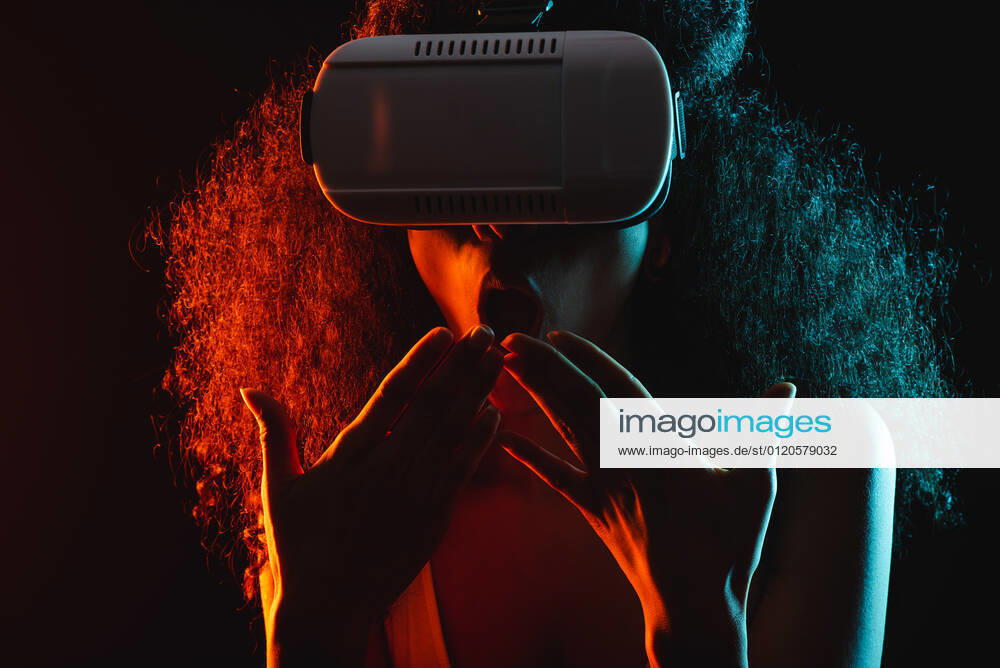 Anonymous astonished ethnic female with open mouth exploring virtual reality in headset on black background, Model released