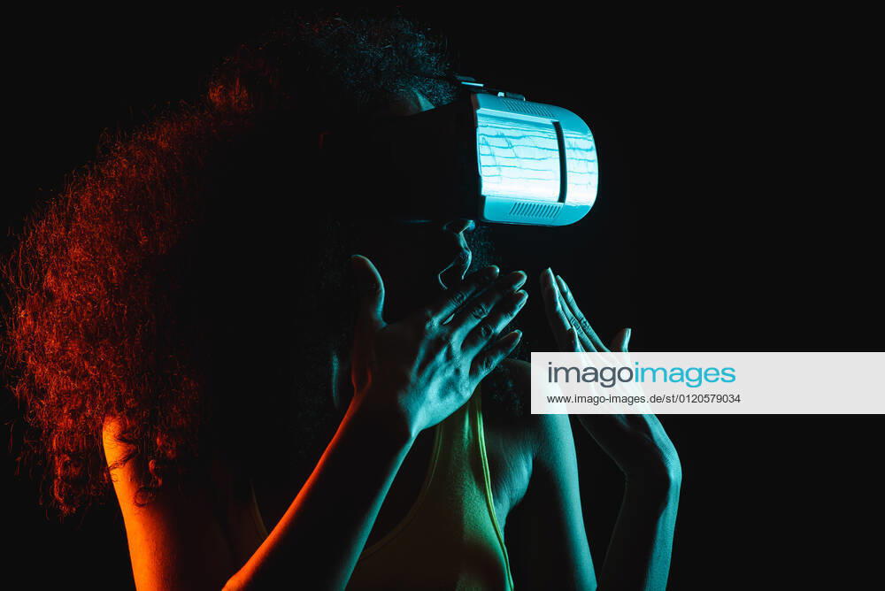 Anonymous astonished ethnic female with open mouth exploring virtual reality in headset on black background, Model released
