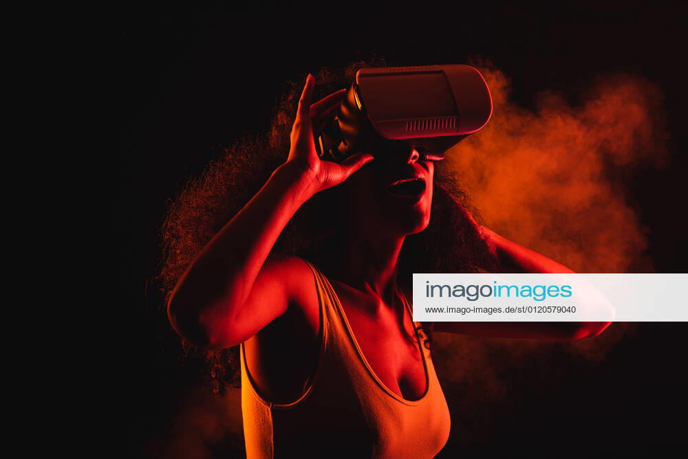 Anonymous astonished ethnic female with open mouth exploring virtual reality in headset on black background, Model released