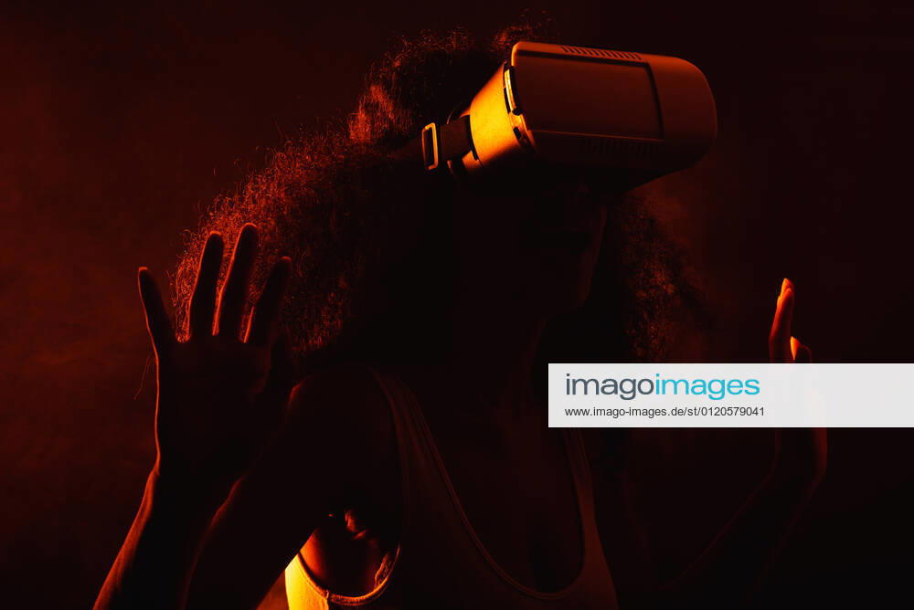 Anonymous astonished ethnic female with open mouth exploring virtual reality in headset on black background, Model released