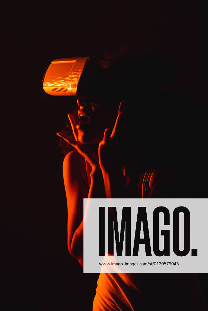 Anonymous astonished ethnic female with open mouth exploring virtual reality in headset on black background, Model released