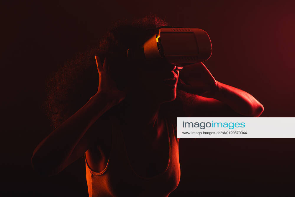Anonymous astonished ethnic female with open mouth exploring virtual reality in headset on black background, Model released