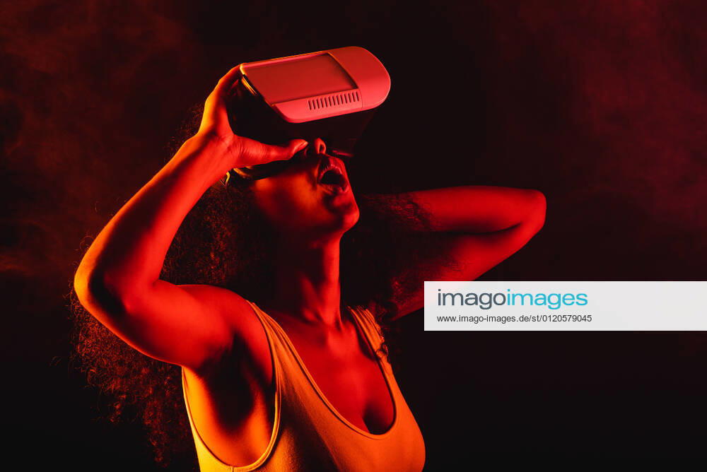 Anonymous astonished ethnic female with open mouth exploring virtual reality in headset on black background, Model released