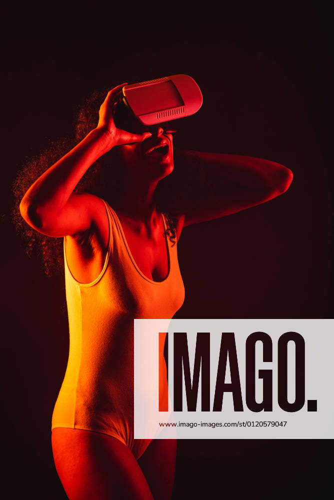 Anonymous astonished ethnic female with open mouth exploring virtual reality in headset on black background, Model released