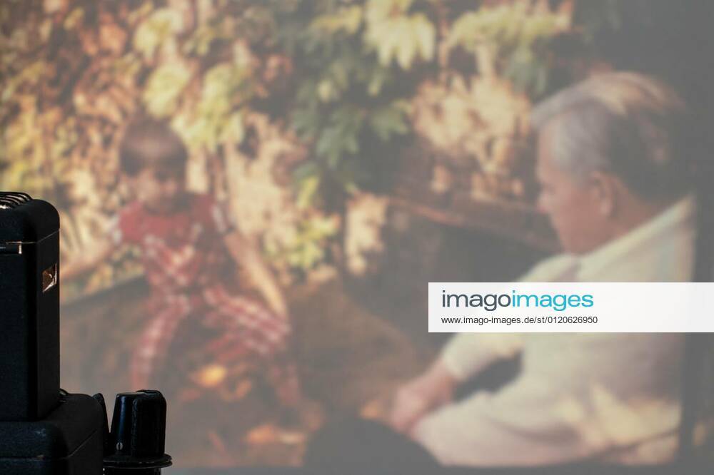 A vintage projector in a dark room enlarges the slides onto a bright projection screen. Entertainment middle of last century to look holiday pictures at home. Macro photograph with focus on projector., 21.02.2020 20:16:51,