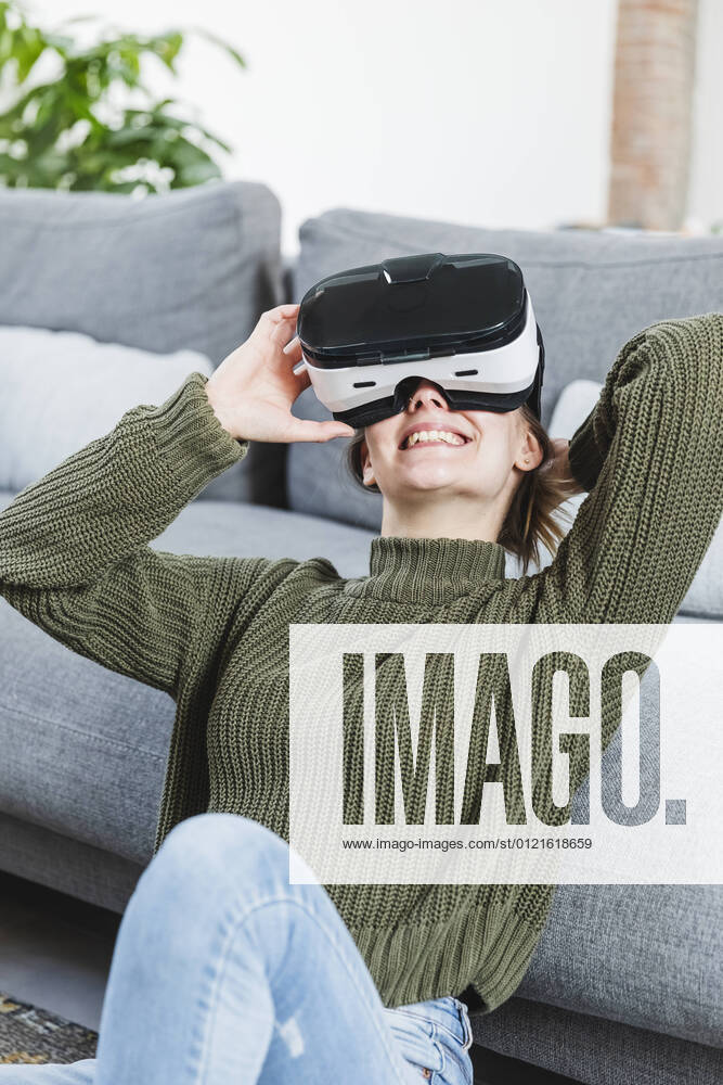 Smiling woman in sweater holding Virtual reality headset at home model released Symbolfoto property released MCVF00801