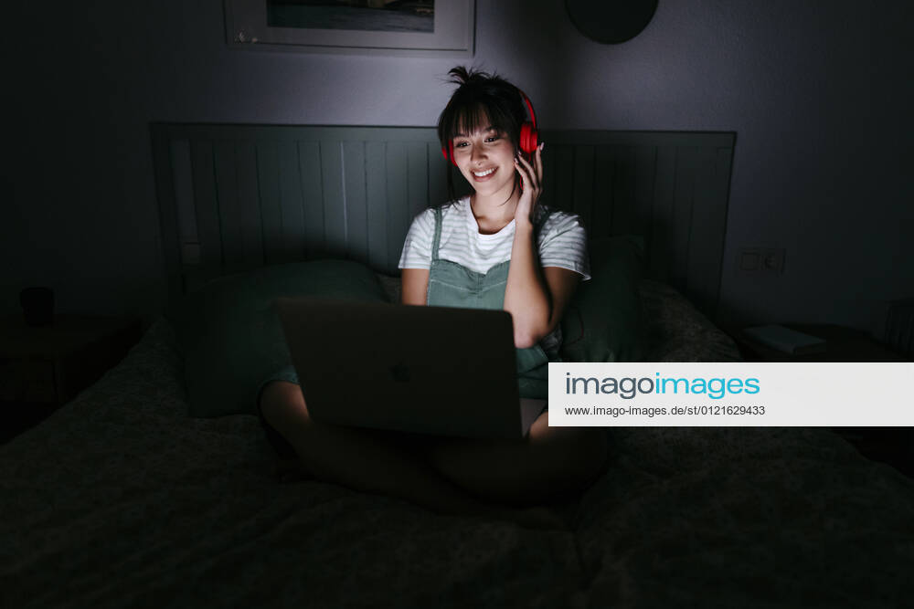 Smiling woman wearing headphones using laptop at home model released Symbolfoto property released TCEF01773