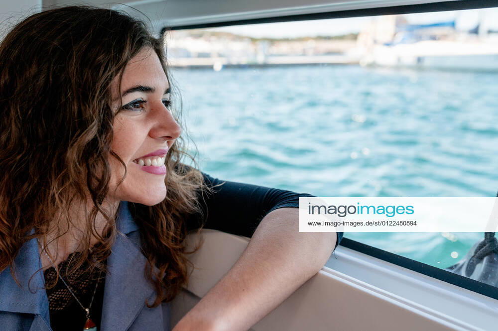 Tranquil female sitting in cabin of catamaran and looking out of window while admiring amazing view of sea on sunny day, Model released, Property released