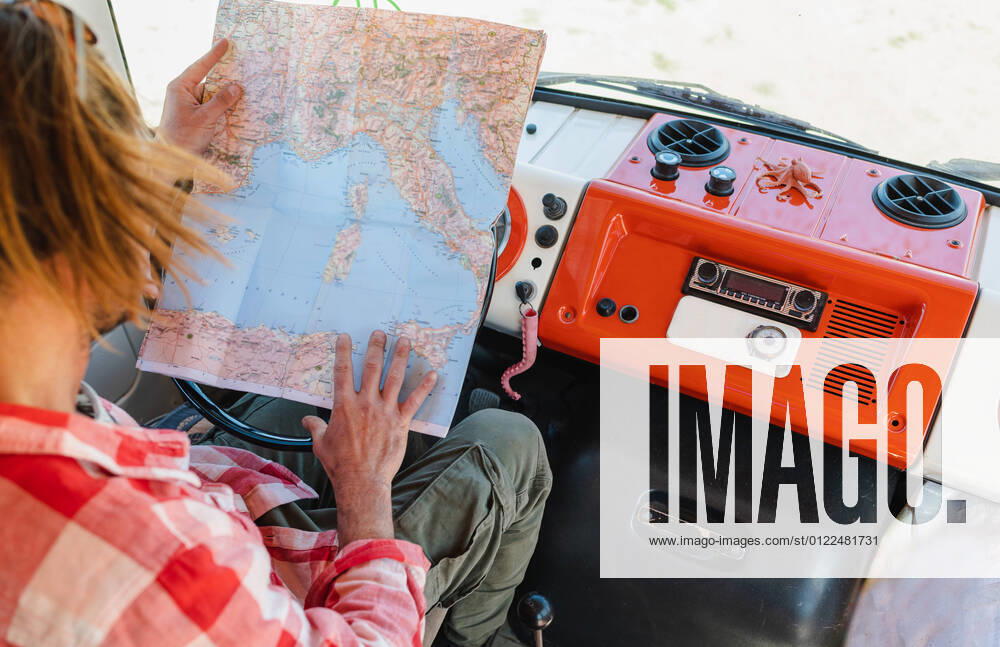 IMAGO Creative: Retro-Revival IMAGO Creative: Digitale Welt, Verzicht auf Technologie From above crop young male traveler in checkered shirt reading map while sitting in retro van during trip in in semi desert valley on sunny day, Model released, Property released