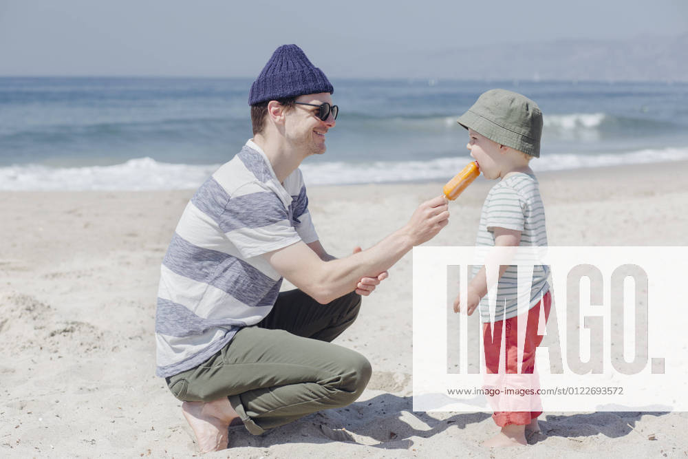 Smiling man feeding ice cream to son at beach during sunny day model released Symbolfoto ACTF00062