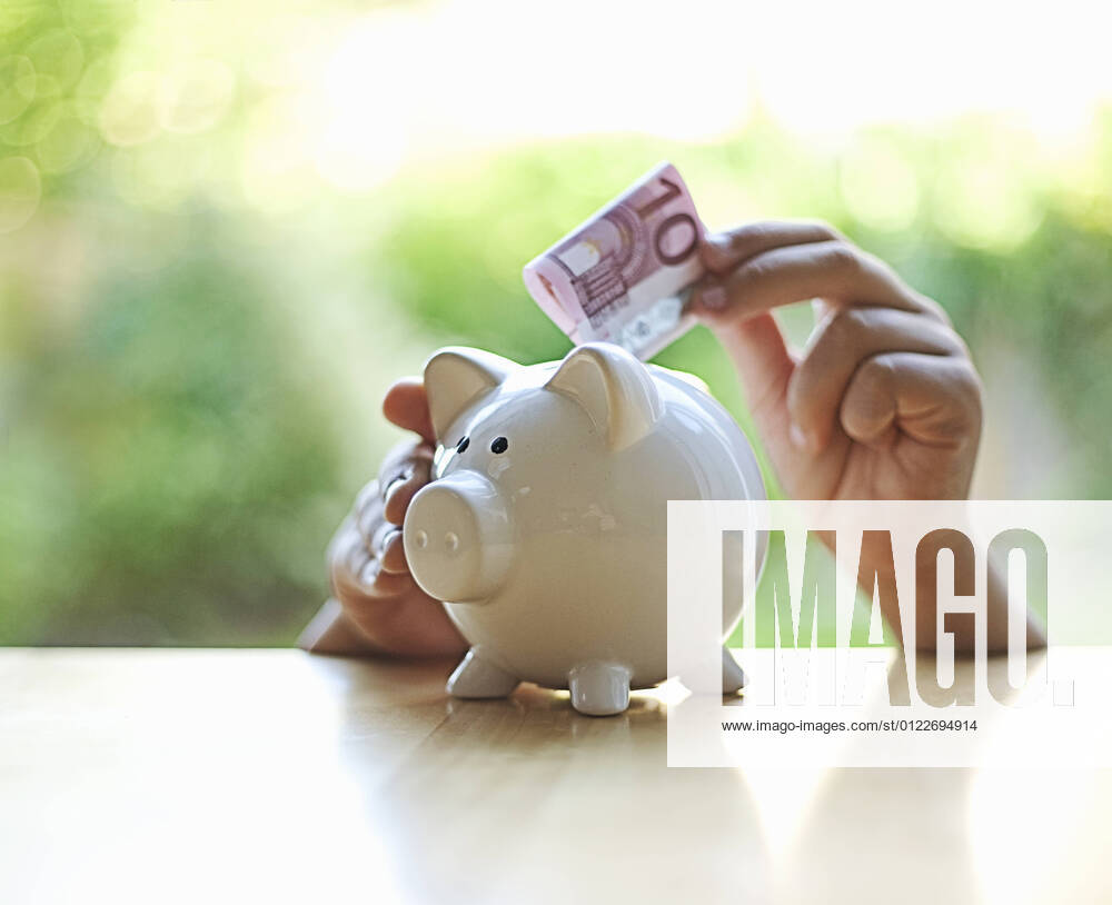 Boy inserting 10 Euro note in piggy bank model released Symbolfoto AJOF01361