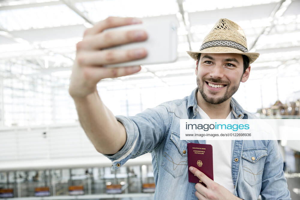 Young man holding passport while taking selfie in airport departure area model released Symbolfoto AUF00739