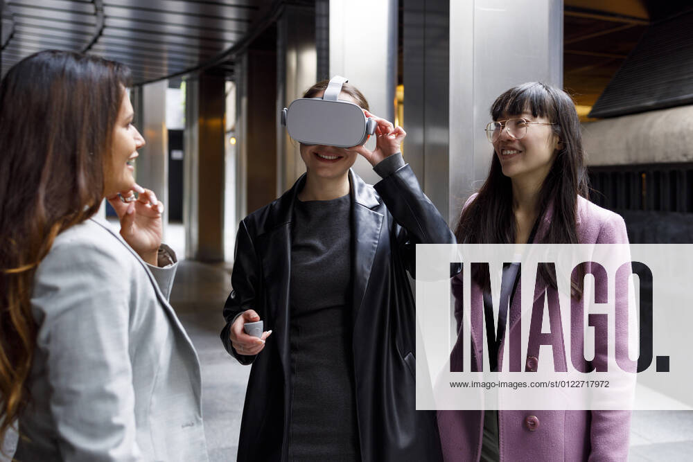 Smiling colleagues looking at businesswoman using virtual reality headset on walkway model released Symbolfoto IFRF00866