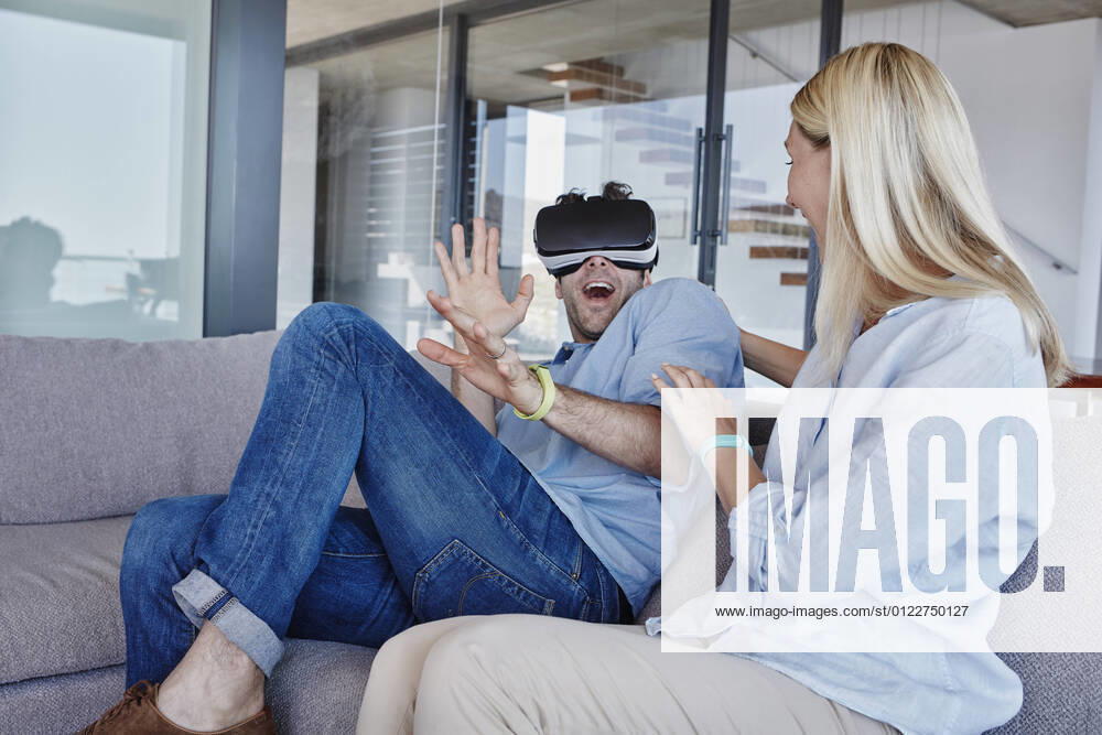 Excited man wearing virtual reality simulator sitting by cheerful woman in living room model released Symbolfoto property released RORF02804