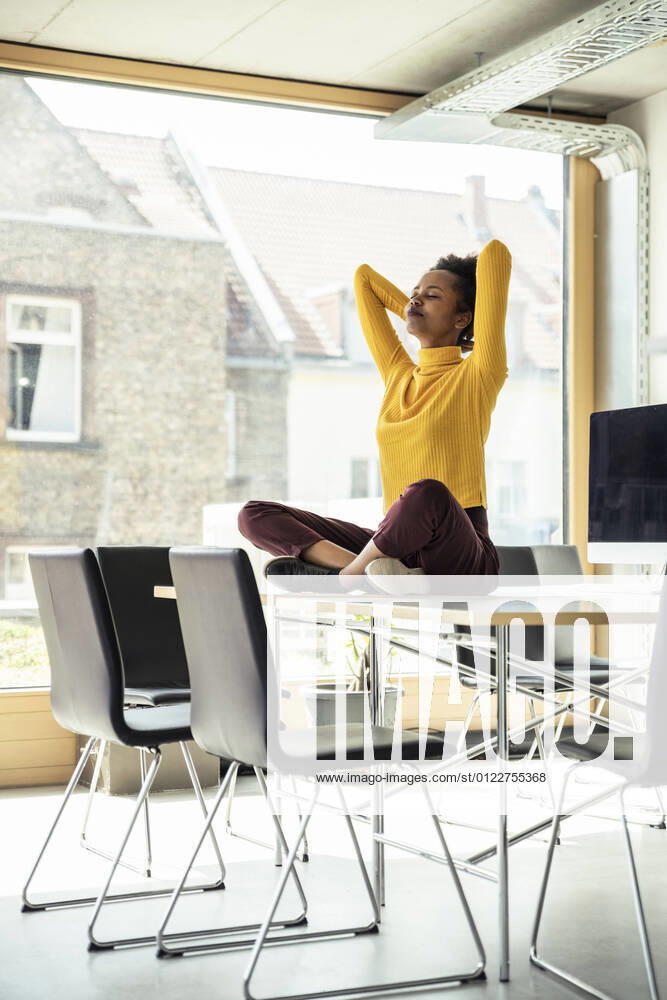 Businesswoman with arms raised meditating on desk at office model released Symbolfoto property released UUF23346