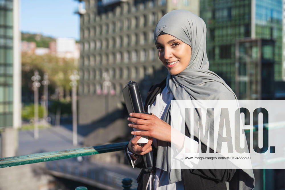 IMAGO Creative: Kreative Renaissance -- der junge Entrepreneur Cheerful Muslim female entrepreneur in hijab and with takeaway coffee standing in street looking at camera, Model released