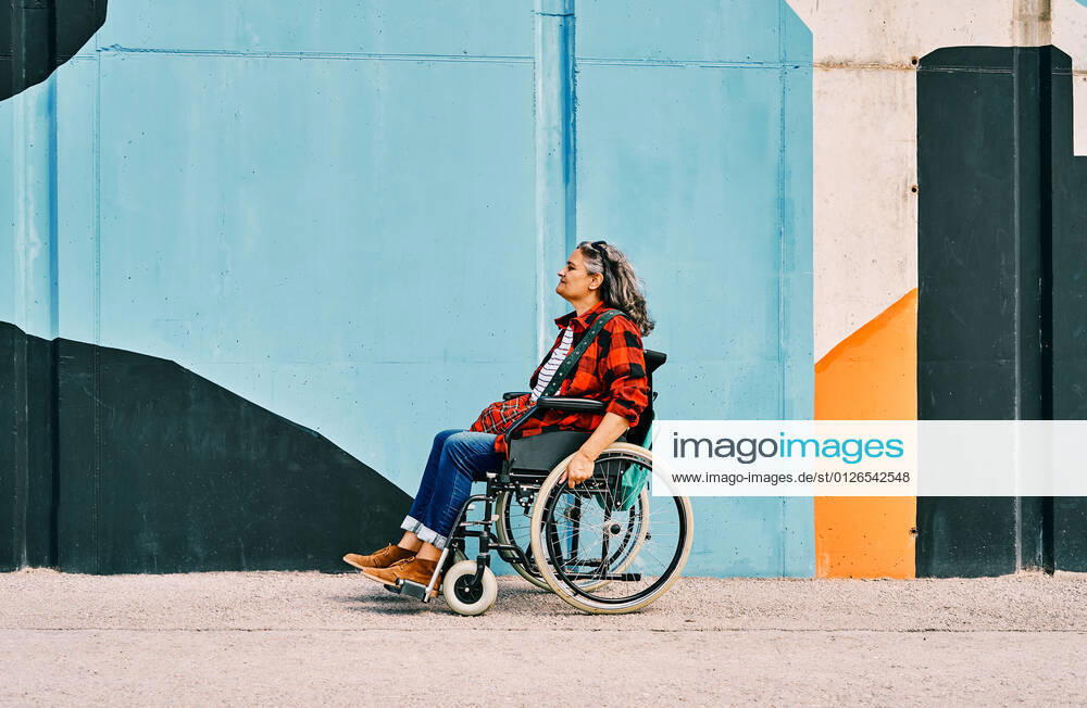 IMAGO Creative, Urban Lifestyle Full body side view of independent handicapped mature female riding wheelchair near painted wall on street, Model released AdalbertoRodriguez_WomanInWheelchairBeach_32.jpg