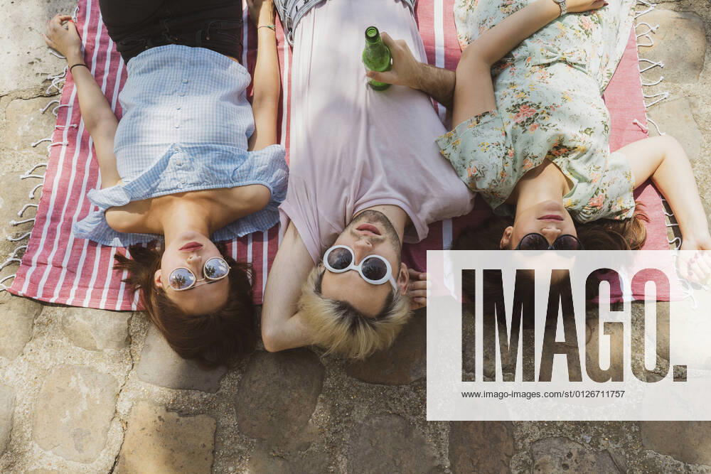 IMAGO Creative: Jahreszeit Frühling, Picknick Male and female friends relaxing on blanket during vacations model released Symbolfoto AFVF08953