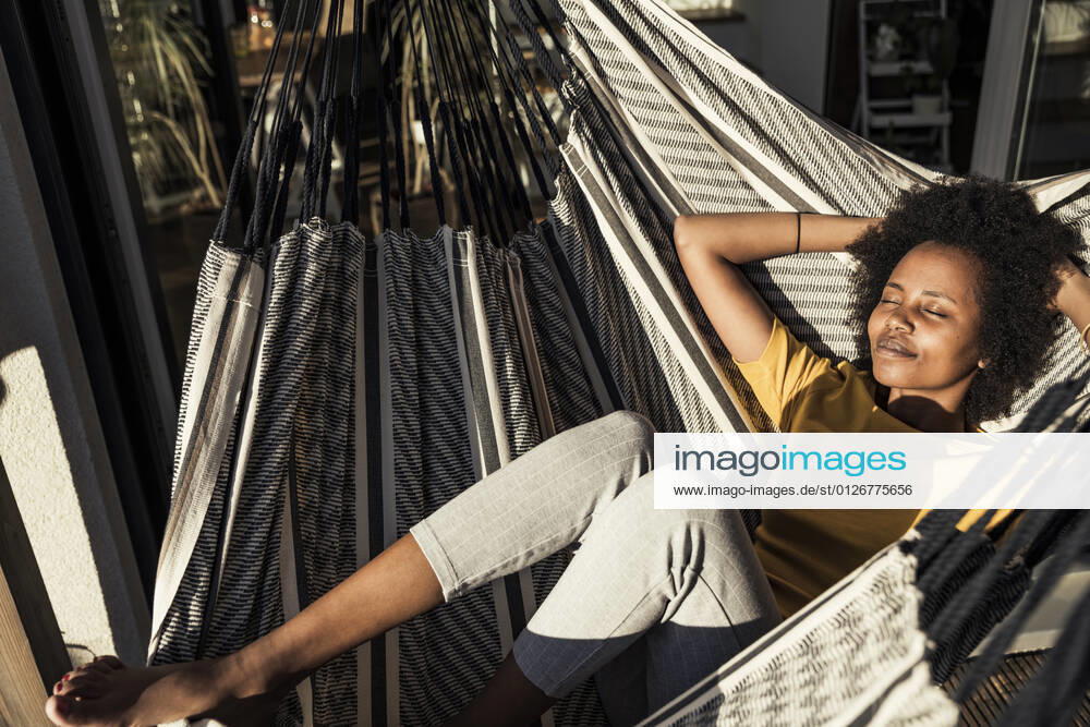 Smiling woman with hands behind head relaxing on hammock during sunny day model released Symbolfoto property released UUF23597