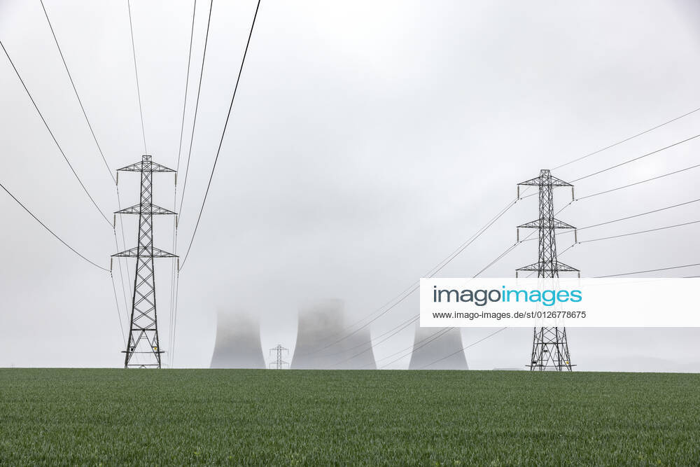 UK, England, Rugeley, Electricity pylons standing in field during foggy weather with cooling towers in background WPEF04930