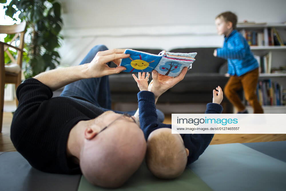 Symbolfoto: Ein Vater spielt mit seinem Baby waehrend im Hintergrund ein zweites Kind tobt. Berlin, 02.02.2021. Berlin Deutschland