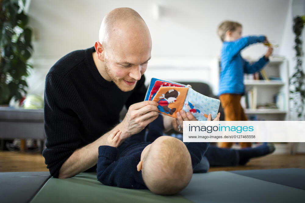 Symbolfoto: Ein Vater spielt mit seinem Baby waehrend im Hintergrund ein zweites Kind fuer sich spielt. Berlin, 02.02.2021. Berlin Deutschland