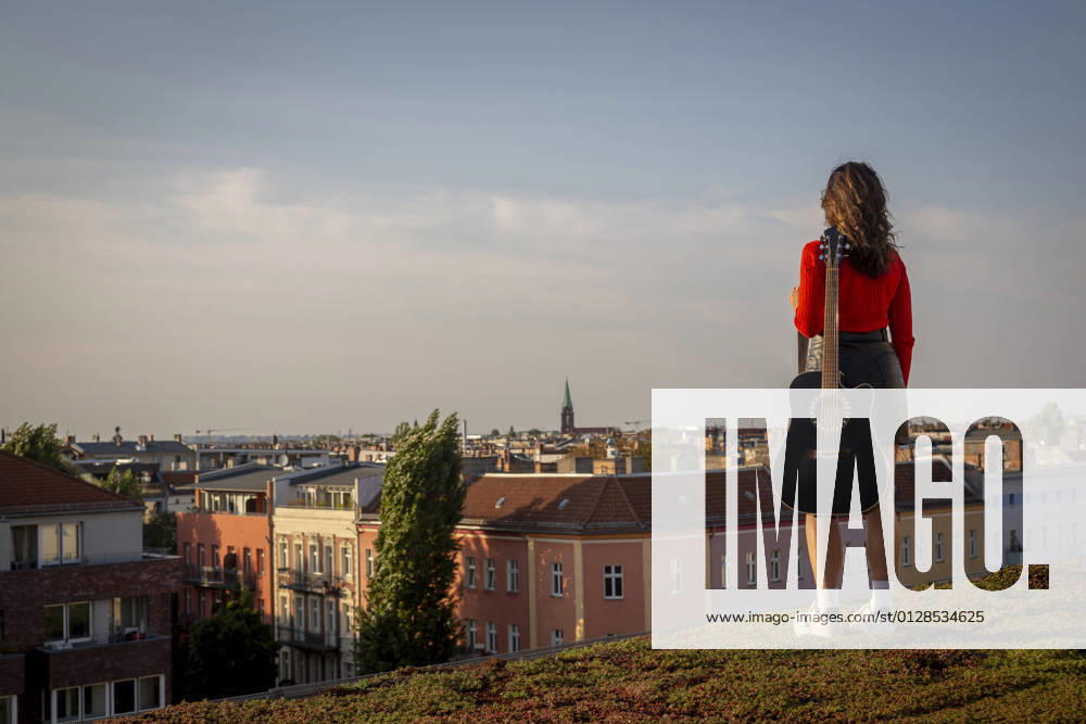 IMAGO Kreativ: Urbane Kultur - Sommer auf den Dächern Young woman carrying guitar while standing on rooftop against sky model released Symbolfoto NGF00701