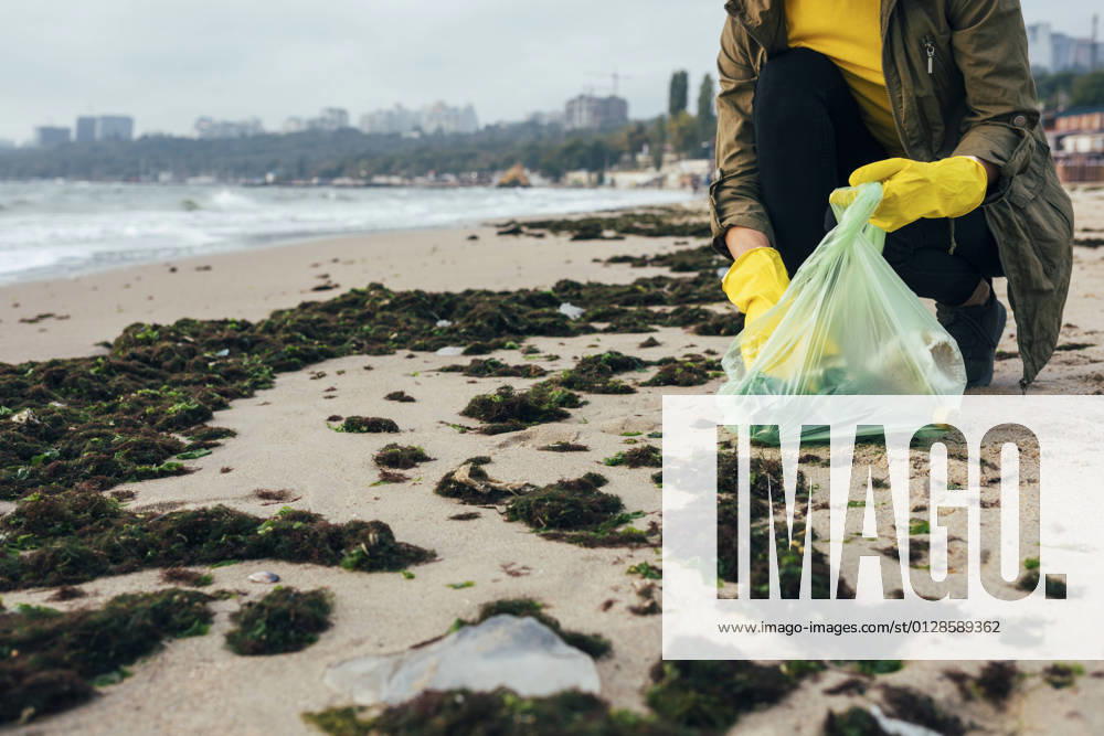 IMAGO Nature: Unsere Erde, Umweltverträgliche Herausforderungen, Plastikmüll Environmentalist collecting garbage in garbage bag while crouching at beach model released Symbolfoto OYF00247