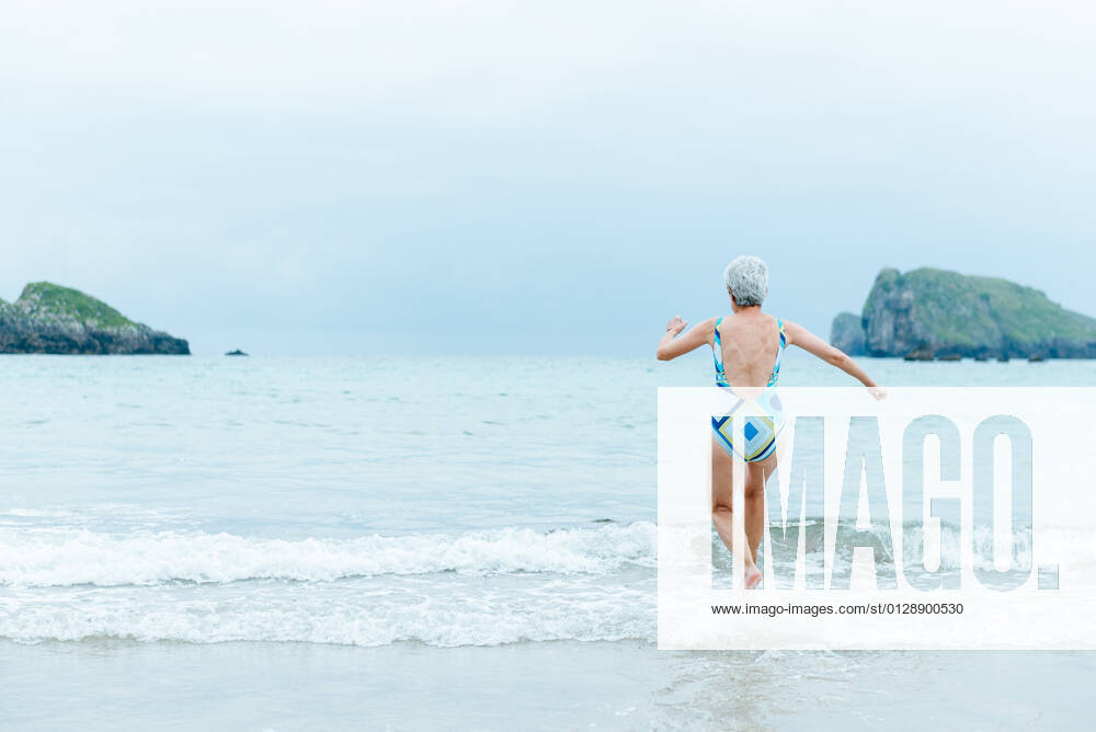 Back view active fit aged female in swimsuit walking on sea water while enjoying summer day on beach, Model released AlbertoMenendez_OldWomanBeach_20.jpg