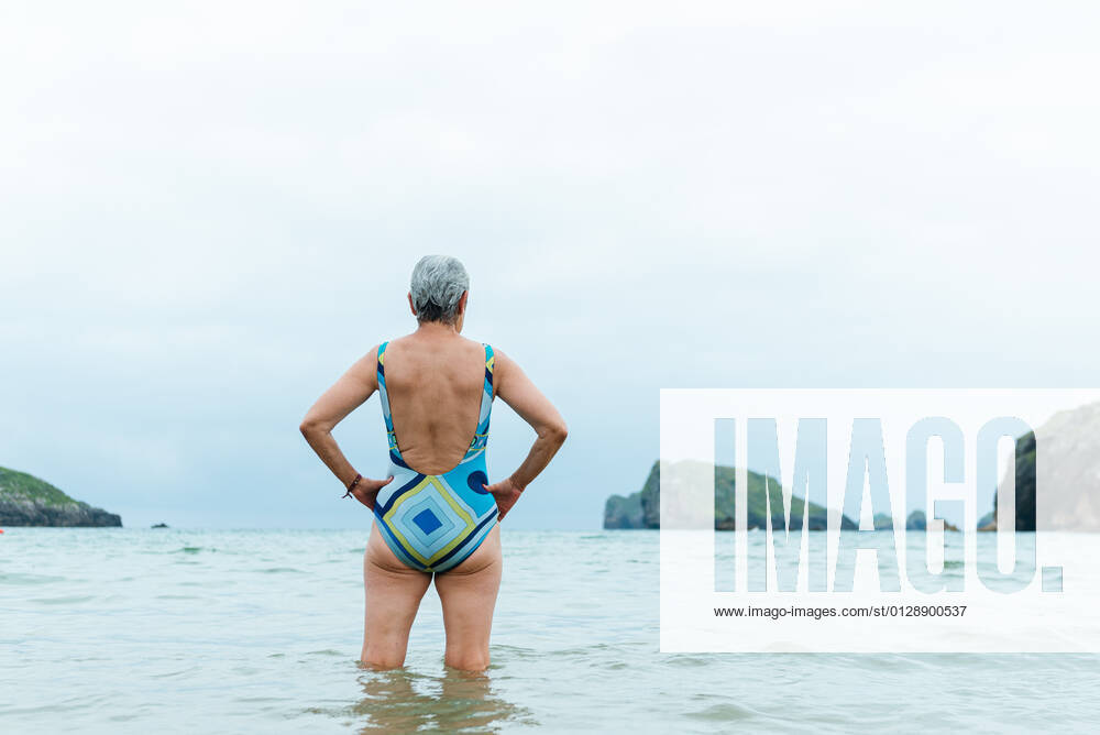 Back view active fit aged female in swimsuit walking out of sea water while enjoying summer day on beach, Model released AlbertoMenendez_OldWomanBeach_26.jpg